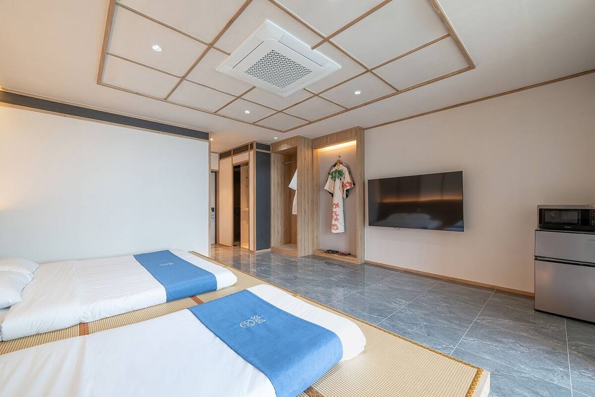 A hotel room with two beds, a flat-screen TV, a microwave, and a refrigerator.