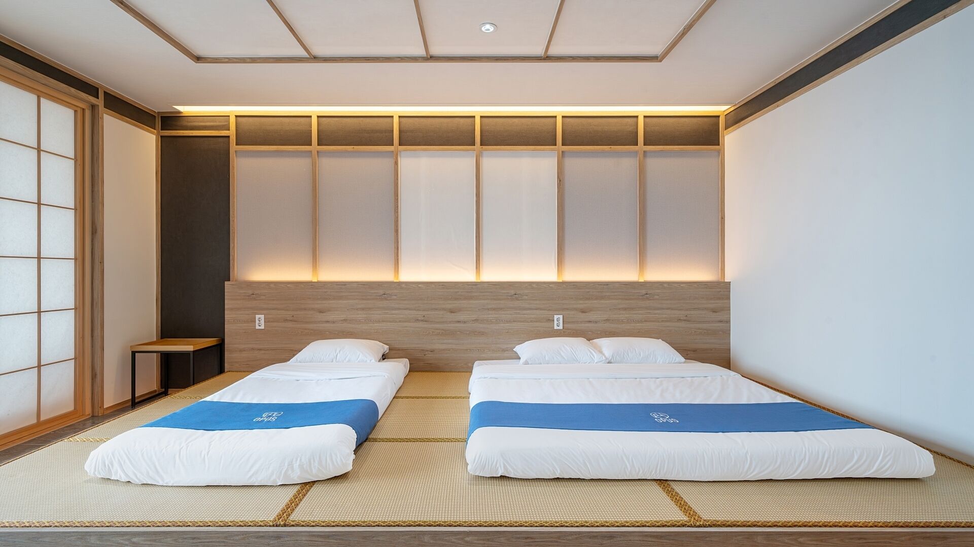 A modern hotel room with two beds, a wooden headboard, and a traditional tatami mat floor.