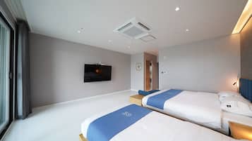 A modern hotel room with two beds, a flat-screen TV mounted on the wall, a ceiling vent, and a door leading to another room.