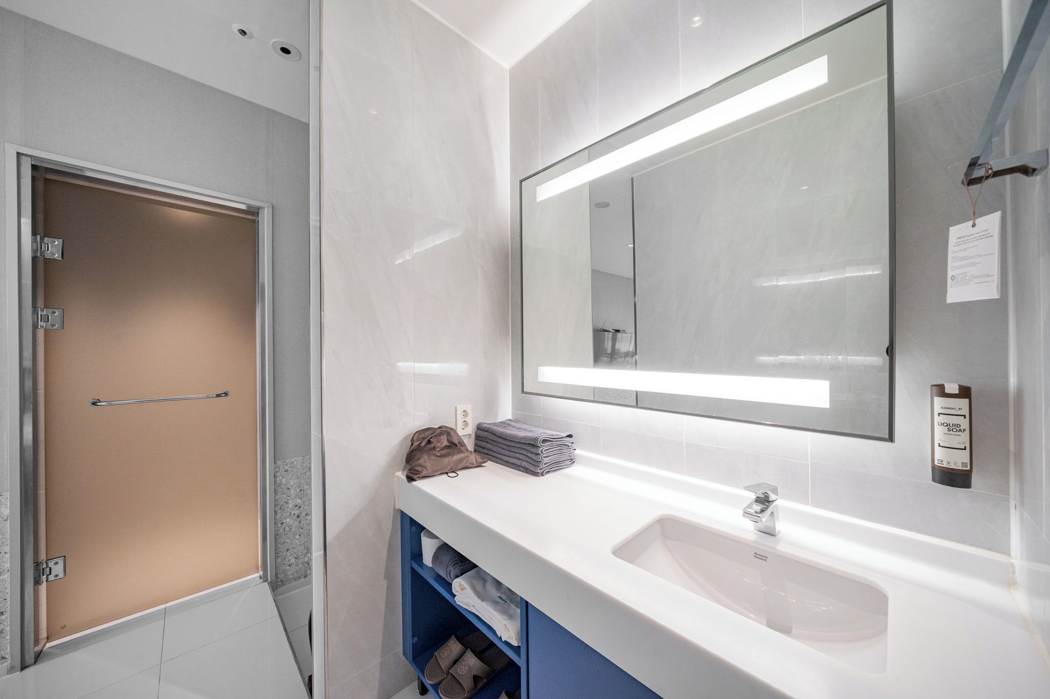 Un baño moderno con un lavamanos blanco, un espejo grande y un perchero para toallas.