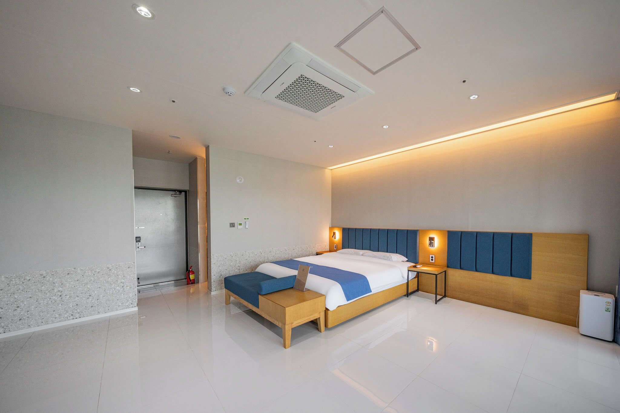 Una habitación de hotel moderna con una cama grande, mesitas de noche, un calentador integrado y una puerta que da a un baño.