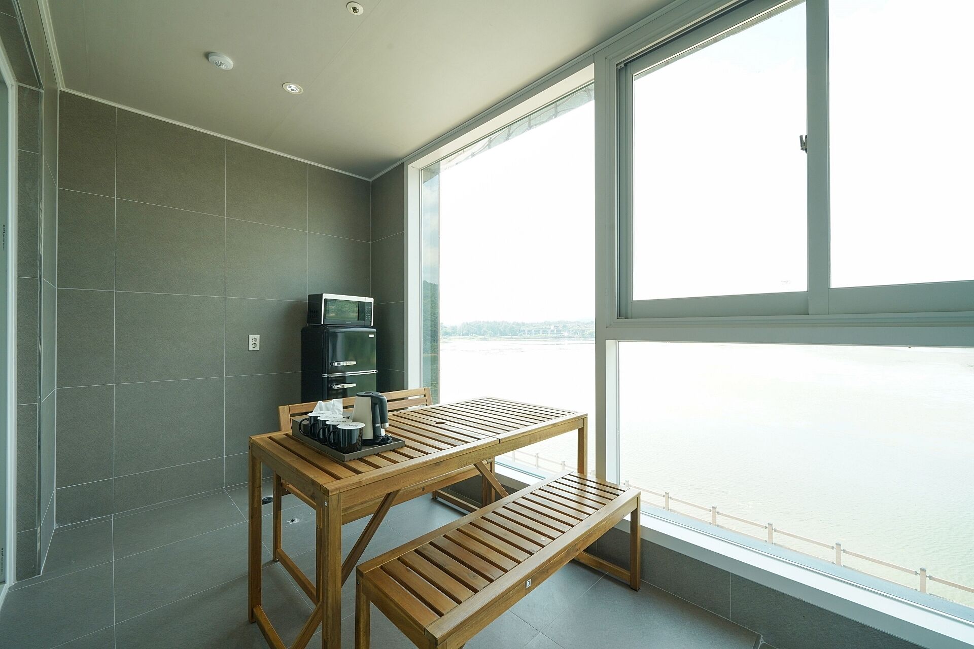 Un balcon avec une table et un banc en bois, un four à micro-ondes et un réfrigérateur.