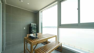 A balcony with a wooden table and bench, a microwave, and a refrigerator.