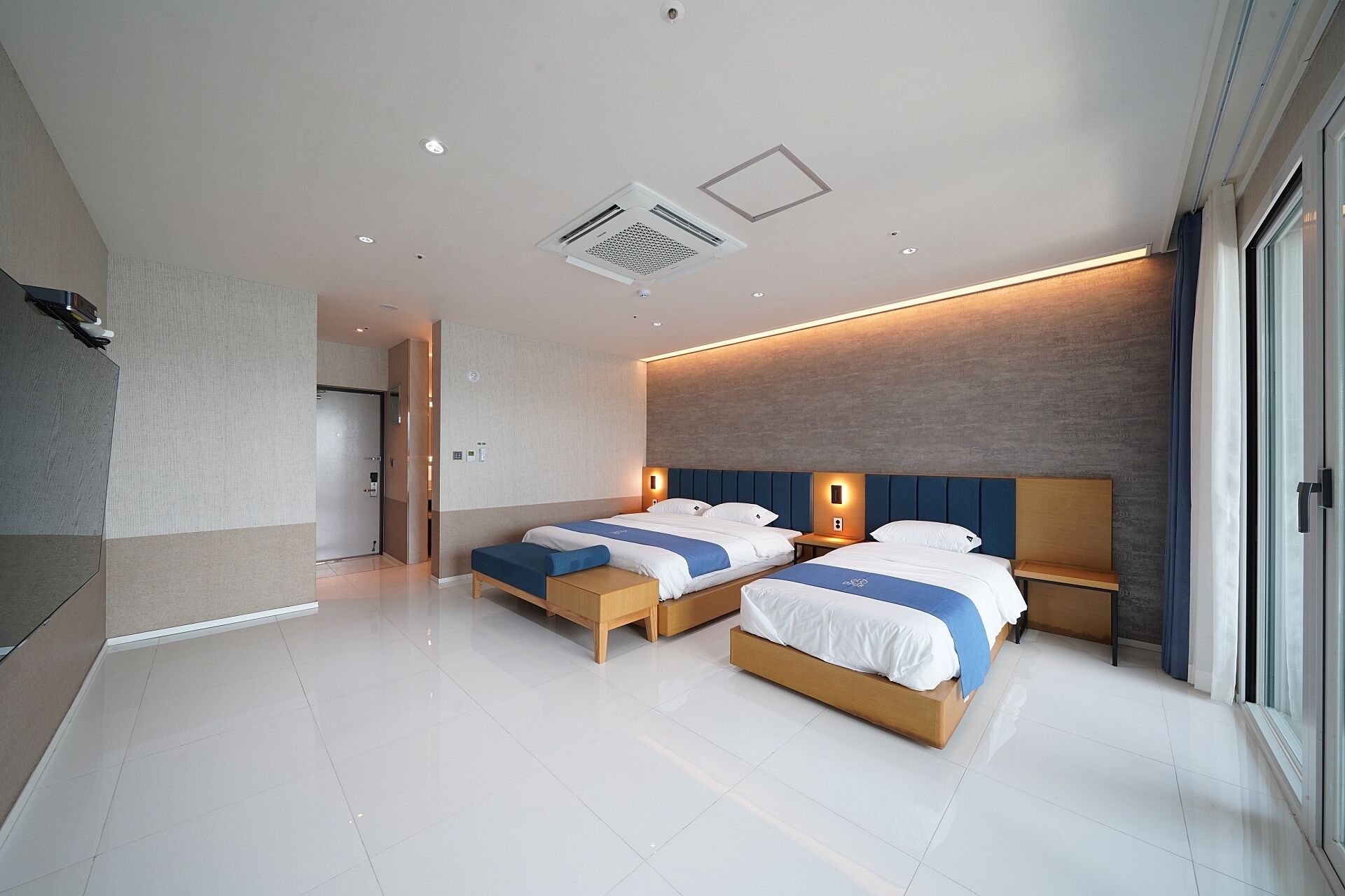 Ein modernes Hotelzimmer mit zwei Betten, einem großen Fenster und einer Decke mit eingelassener Beleuchtung.