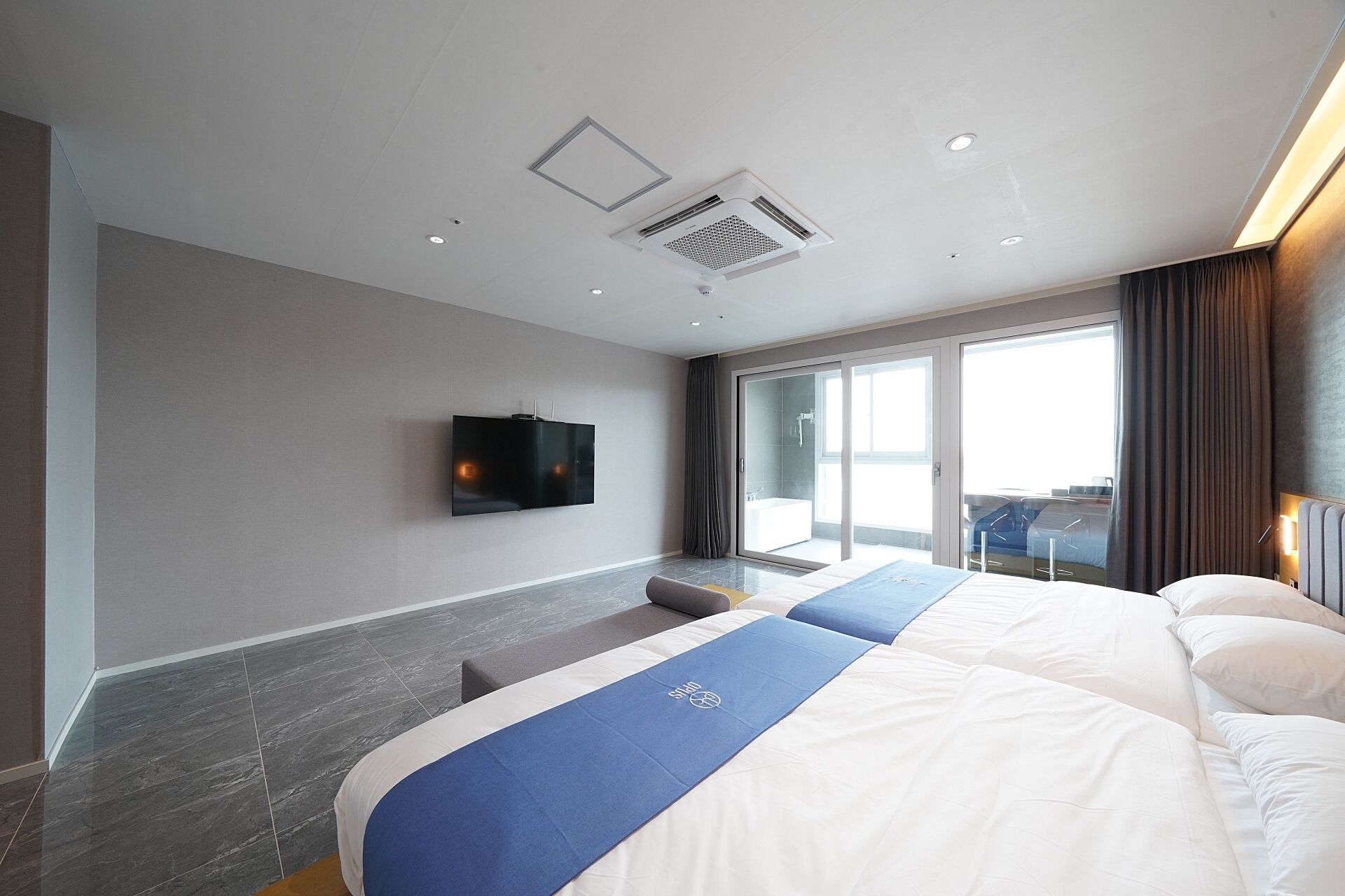 Una habitación de hotel moderna con una cama grande, un televisor de pantalla plana en la pared y un ventanal corredero que da a un balcón.