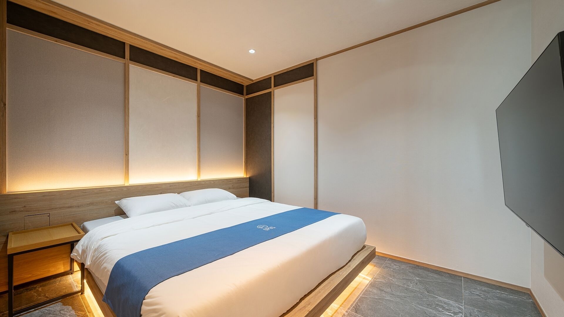 A modern hotel room with a large bed, wooden headboard, and a nightstand.