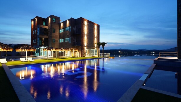 Un hotel moderno con piscina infinita en la azotea, sillas de descanso y vistas a la montaña.
