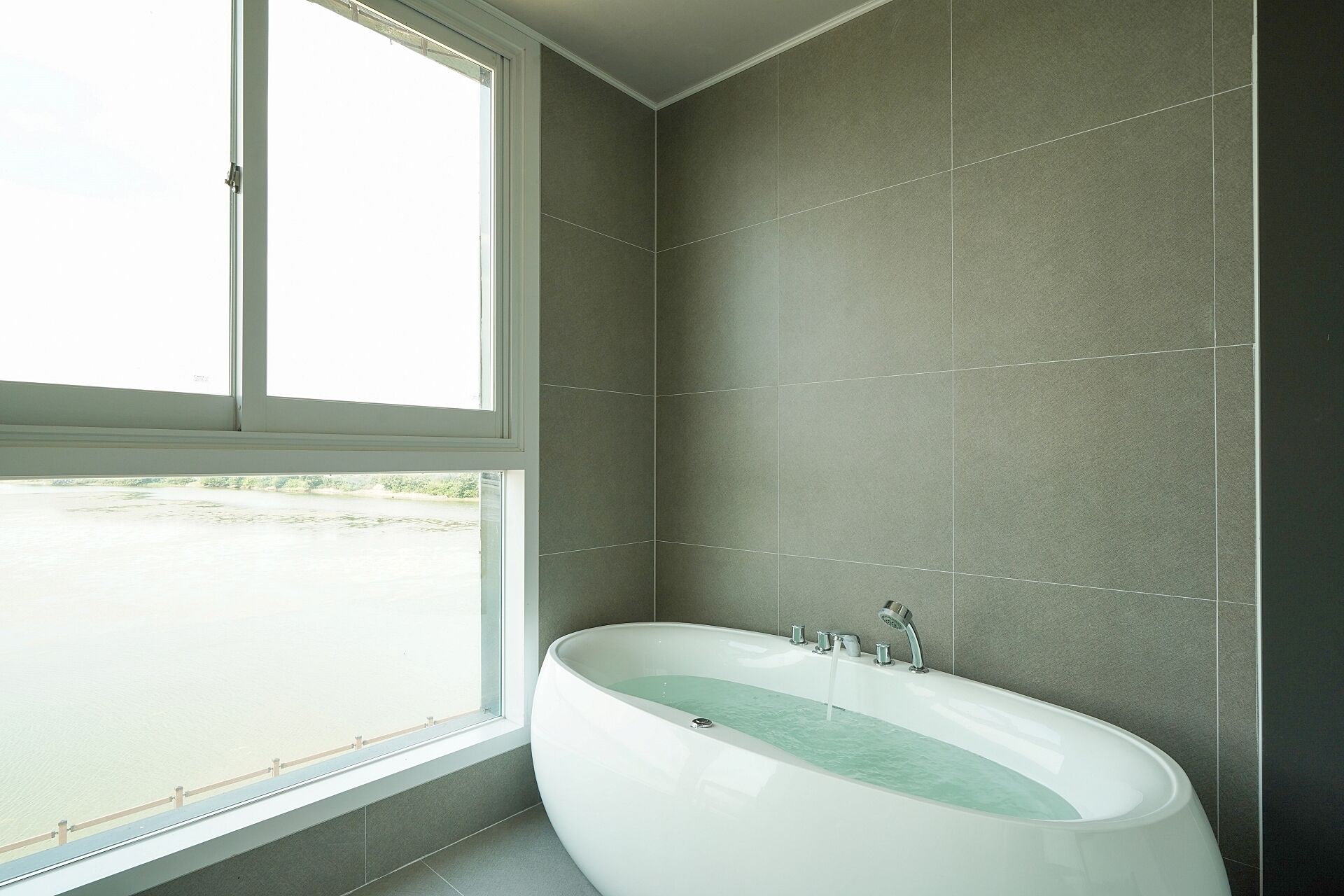 Une salle de bain moderne avec une baignoire sur pieds, de grandes fenêtres et des murs recouverts de carreaux gris.