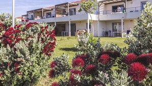 A hotel with multiple balconies, a well-maintained lawn, and red flowering plants in the foreground. - Résidence Odalys Référence Acqua Bella by Interhome (Moriani-Plage)
