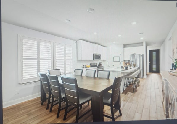 A modern kitchen with white cabinets, a central island, and a dining area with a long table and chairs.