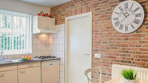 A kitchen with white cabinets, a brick wall, a clock, and a dining area with a table and chairs.