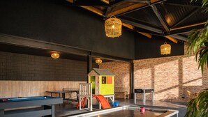 A billiards table with balls, a children's play area, and a brick wall.