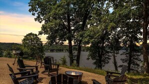 An outdoor seating area with Adirondack chairs and a fire pit, overlooking a lake. - 17 Lakefront Acres, Private Dock, Firepit, Pool Table, Kayaks, Fishing (Gravois Mills)