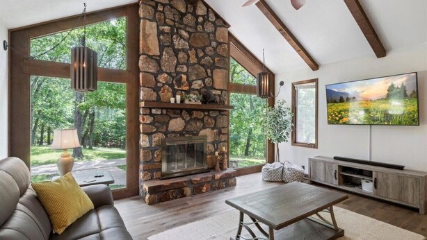 A cozy living room with a stone fireplace, large windows, a comfortable sofa, and a flat-screen TV. - 17 Lakefront Acres, Private Dock, Firepit, Pool Table, Kayaks, Fishing (Gravois Mills)