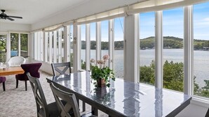 A dining area with a view of a lake and hills, featuring a table, chairs, and a ceiling fan. - 17 Lakefront Acres, Private Dock, Firepit, Pool Table, Kayaks, Fishing (Gravois Mills)