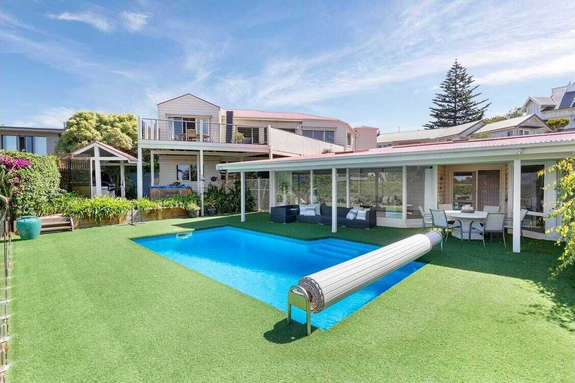 En swimmingpool med et nedsænket spabad, omgivet af en overdækket terrasse med udendørs møbler.