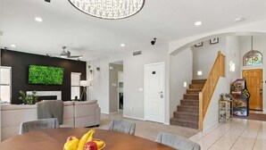 A modern living room with a flat-screen TV, a dining table with fruit, a staircase, and a fireplace.