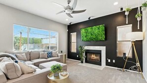 A modern living room with a sofa, fireplace, ceiling fan, and large windows.