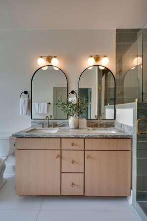 Une salle de bain avec un meuble-lavabo à deux vasques, deux miroirs fixés au mur et un espace douche.