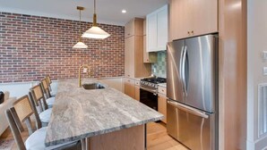 Una cocina moderna con pared de ladrillo, electrodomésticos de acero inoxidable y una isla central con asientos.