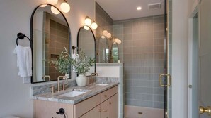 Un baño moderno con tocador, dos lavamanos, un espejo grande y cabina de ducha con mampara de cristal.