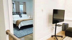 A bedroom with a bed, a television on a stand, and a small rug.