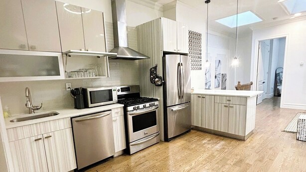 A modern kitchen with white cabinetry, stainless steel appliances, and a wooden floor.