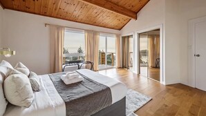 A bedroom with a large bed, a wooden ceiling, and a balcony with a view. - Ocean's Embrance Suite (Nanaimo)