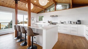 A modern kitchen with a central island, bar stools, and a view of the outdoors. - Ocean's Embrance Suite (Nanaimo)