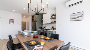 A modern kitchen with a dining area, featuring a chandelier, a refrigerator, and a coffee maker.