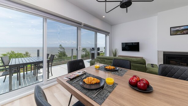 A modern dining area with a large table, breakfast items, and a view of the sea.