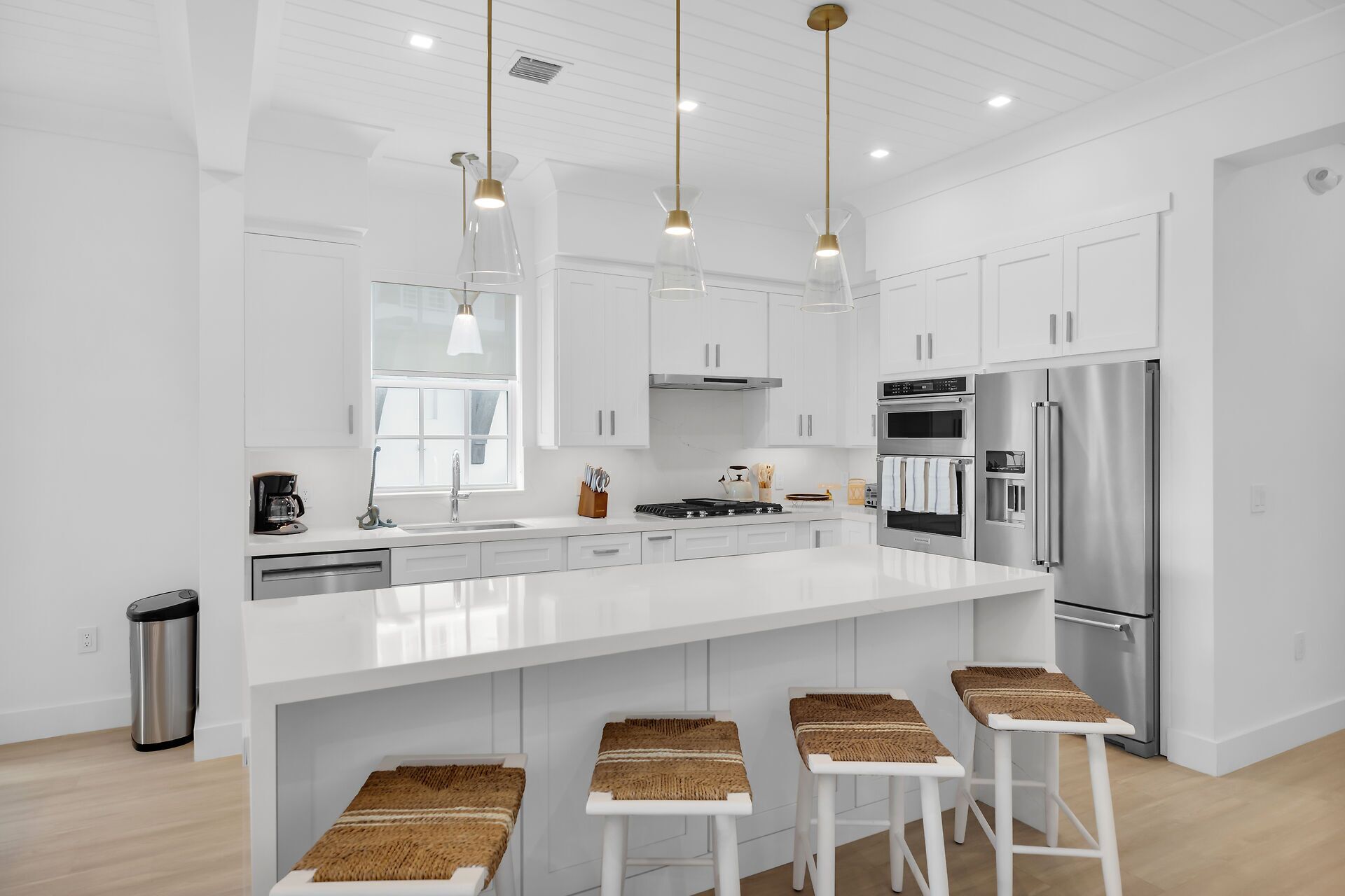 Una cocina moderna con armarios blancos, electrodomésticos de acero inoxidable y una isla central con taburetes de bar.