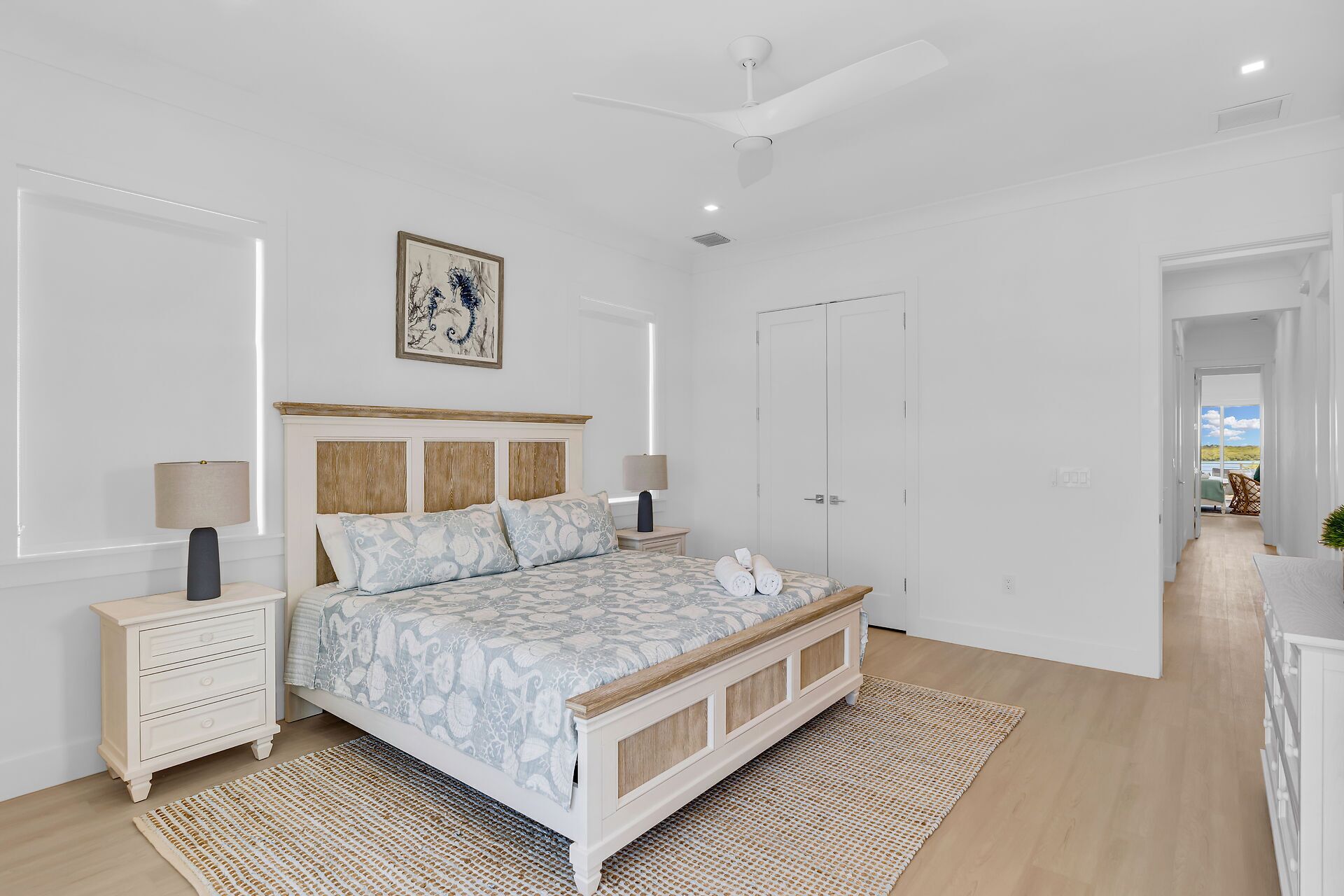 A bedroom with a bed, bedside tables, a ceiling fan, a door, and a view through an open door.