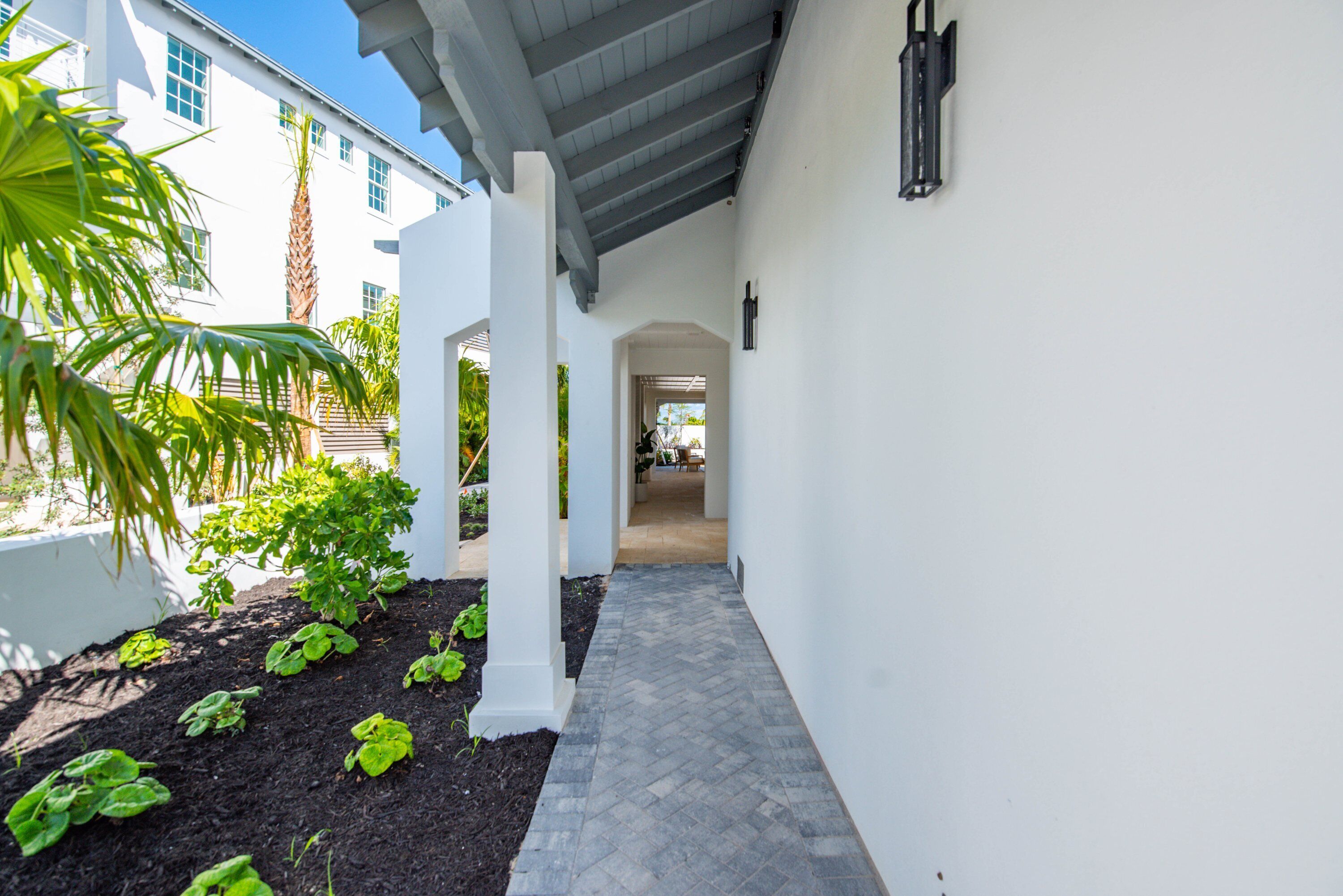 A covered pathway leading to a building with white walls and a tiled floor.