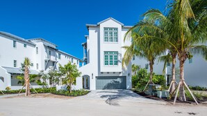 A modern white building with a garage, surrounded by palm trees and a clear blue sky. - Sea Glass Cove (Marathon)