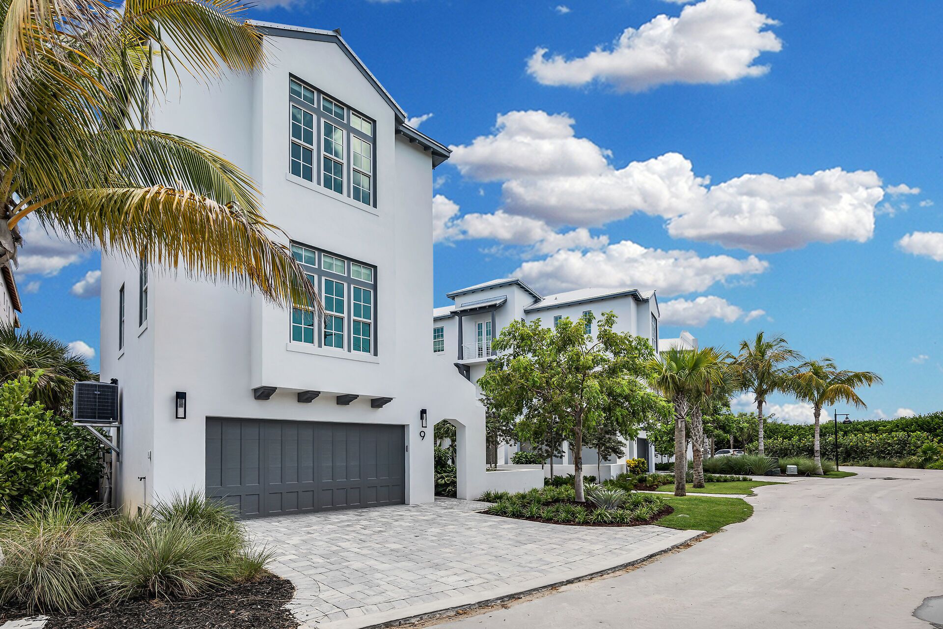 A modern two-story house with a garage, surrounded by well-maintained landscaping and palm trees.