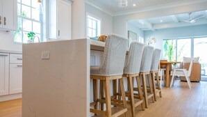 A modern kitchen with white cabinetry, a marble island, and wooden bar stools. - Sea Glass Cove (Marathon)