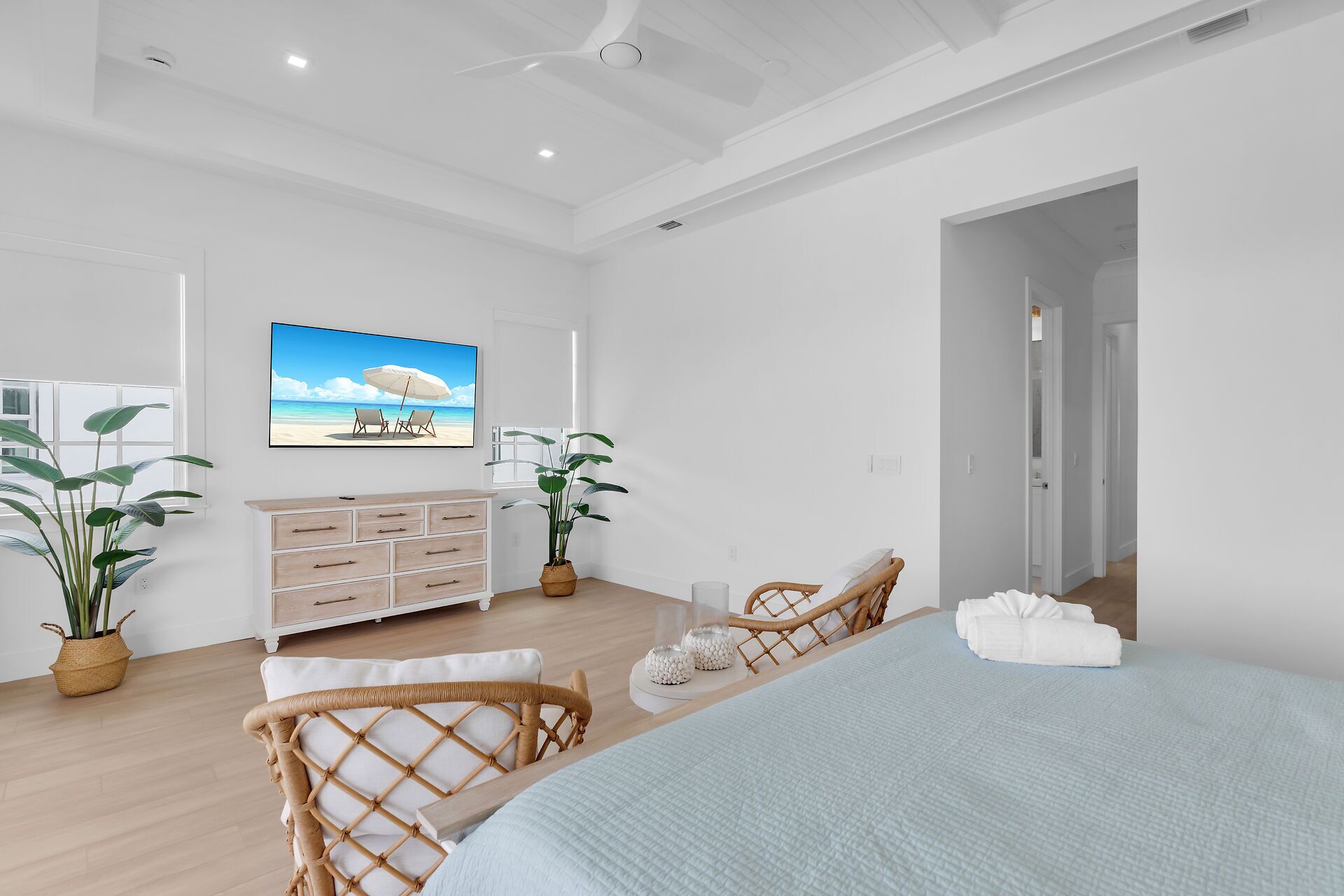 Une chambre à coucher avec un lit, une commode, un fauteuil en osier et une grande fenêtre.