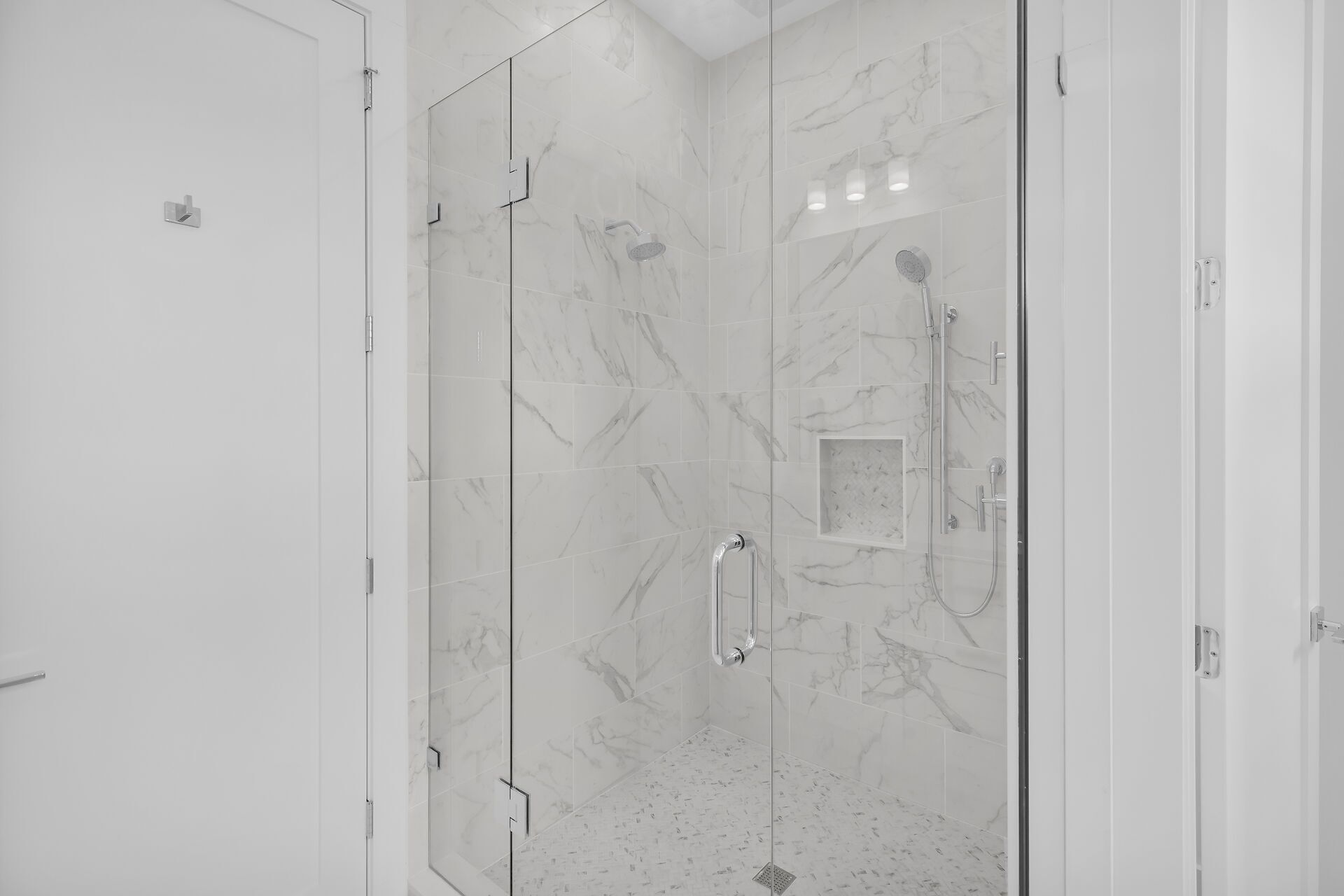 A modern bathroom with a glass-enclosed shower area, marble tiles, and a small shelf with toiletries.