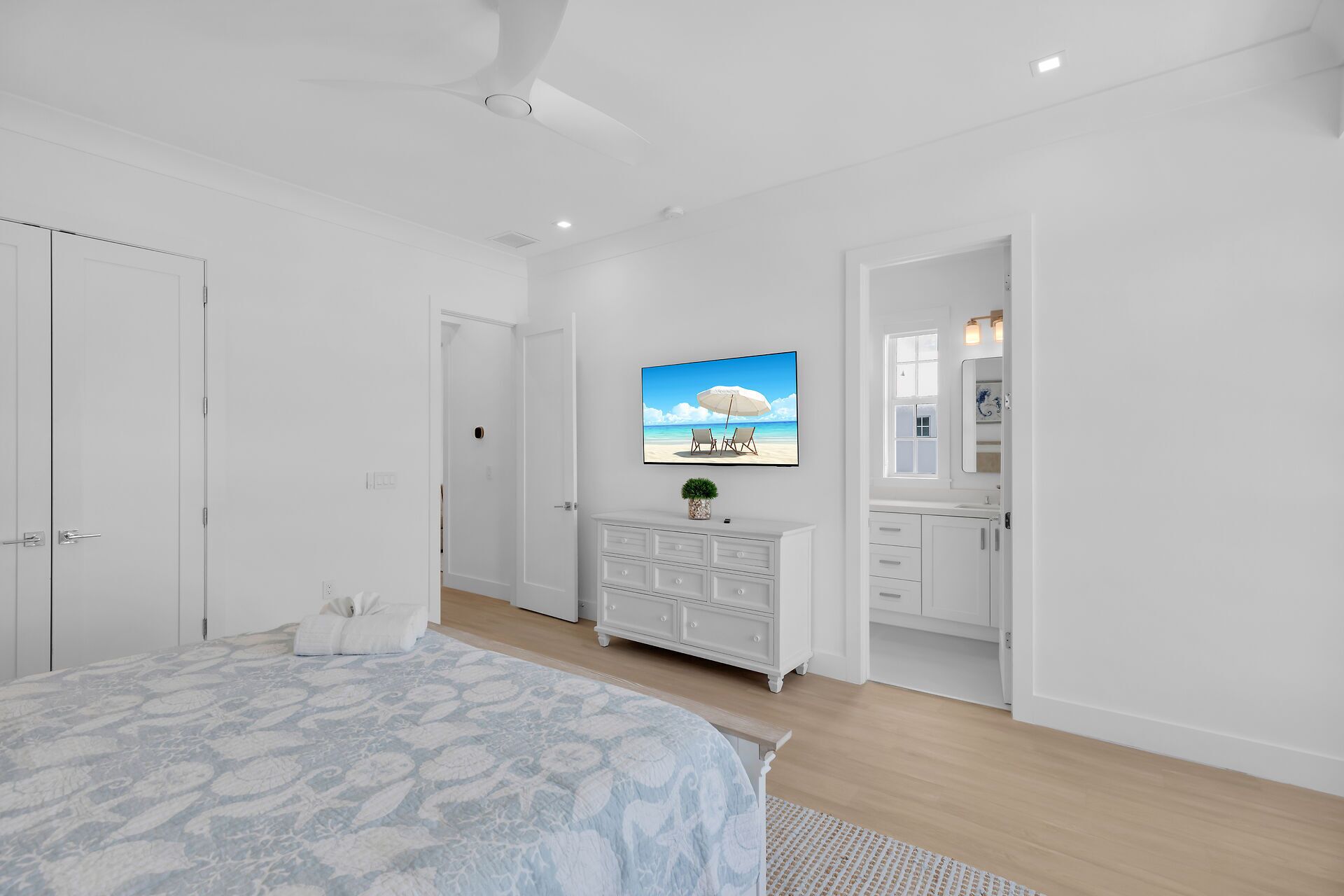A bedroom with a bed, a dresser, a TV, and a bathroom with a mirror and sink.