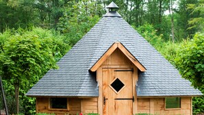 Een klein houten huisje met een steile dakschild en een deur in het midden, plus een klein raam aan de zijkant.
