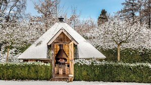 Een houten hutje met een rieten dak, omgeven door met sneeuw bedekte bomen en een haag.