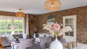 Un salon moderne avec un mur en briques, des canapés gris, un vase blanc orné de fleurs et une table à manger en bois.
