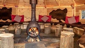 Un poêle à bois dans une cabane en bois, avec des tapis en fourrure aux murs et un sol en pierre.