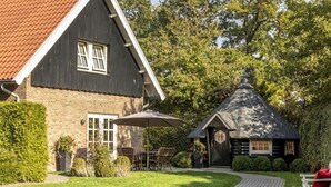 Une maison traditionnelle avec une façade en briques, un toit en tuiles et une petite dépendance attenante surmontée d’un toit conique.