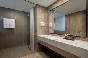 A modern bathroom with a shower, two sinks, a large mirror, and a towel rack with a towel labeled "ASTON". - Aston Inn Lumajang - East Java (Lumajang)