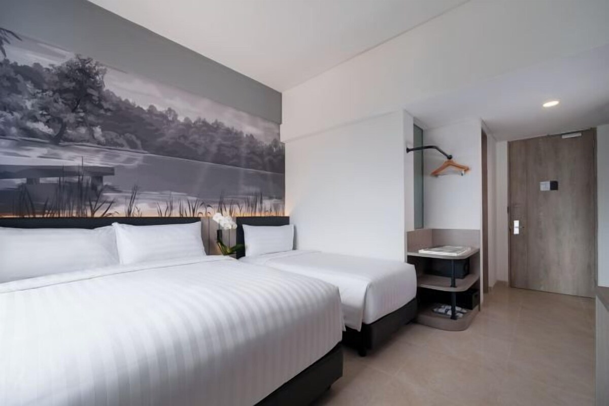 A modern hotel room with a large bed, a small bedside table, a nightstand, a wall-mounted shelf, and a door.
