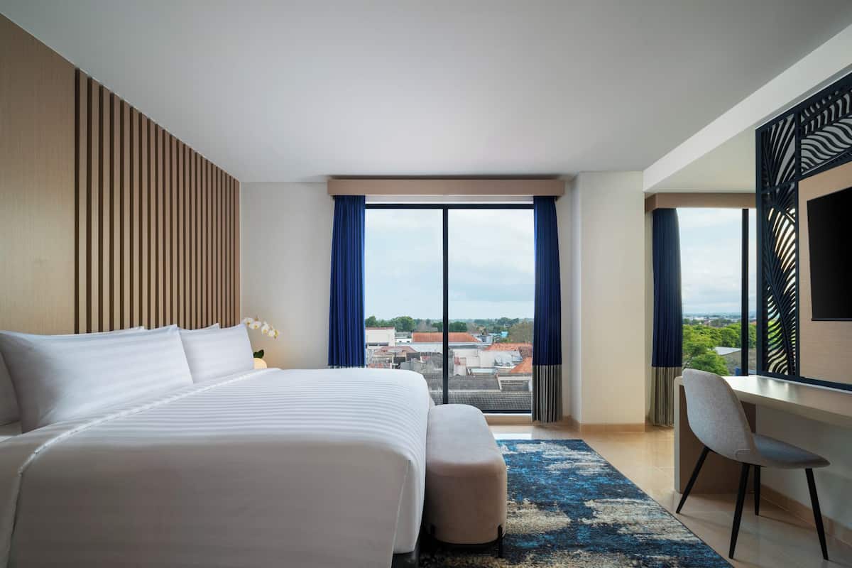 A modern hotel room with a large bed, a desk, and a view of the city.