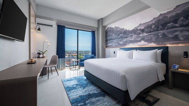Une chambre d’hôtel moderne dotée d’un grand lit, d’un bureau, d’une chaise, d’une télévision et offrant une vue sur le paysage urbain.