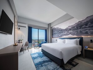 A modern hotel room with a large bed, a desk, a chair, a TV, and a view of a cityscape. - Aston Inn Lumajang - East Java (Lumajang)